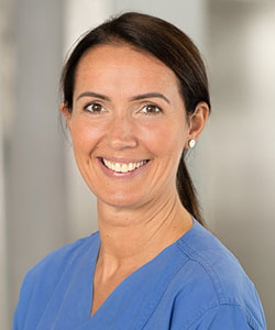 Braunhaarige Kinderkrankenschwester mit Zopf und Ohrstecker trägt blauen Kittel und lächelt mit Zähnen