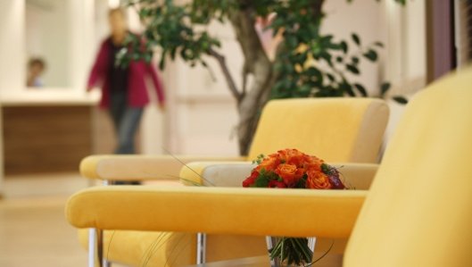 Symbolbild: zwei Sessel, Tischchen mit Blumenstrauß, verschwommener Hintergrund. 