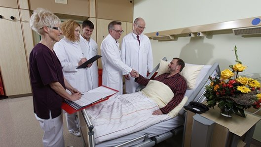 Symbolbild: Vier Ärzte und eine Pflegekraft bei einer Visite am Krankenbett mit einem Patienten im Bett.