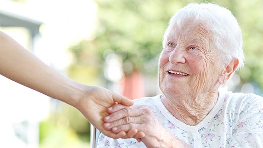 Eine ältere Dame hät mit einem Lächeln eine ihr hingehaltene Hand. 